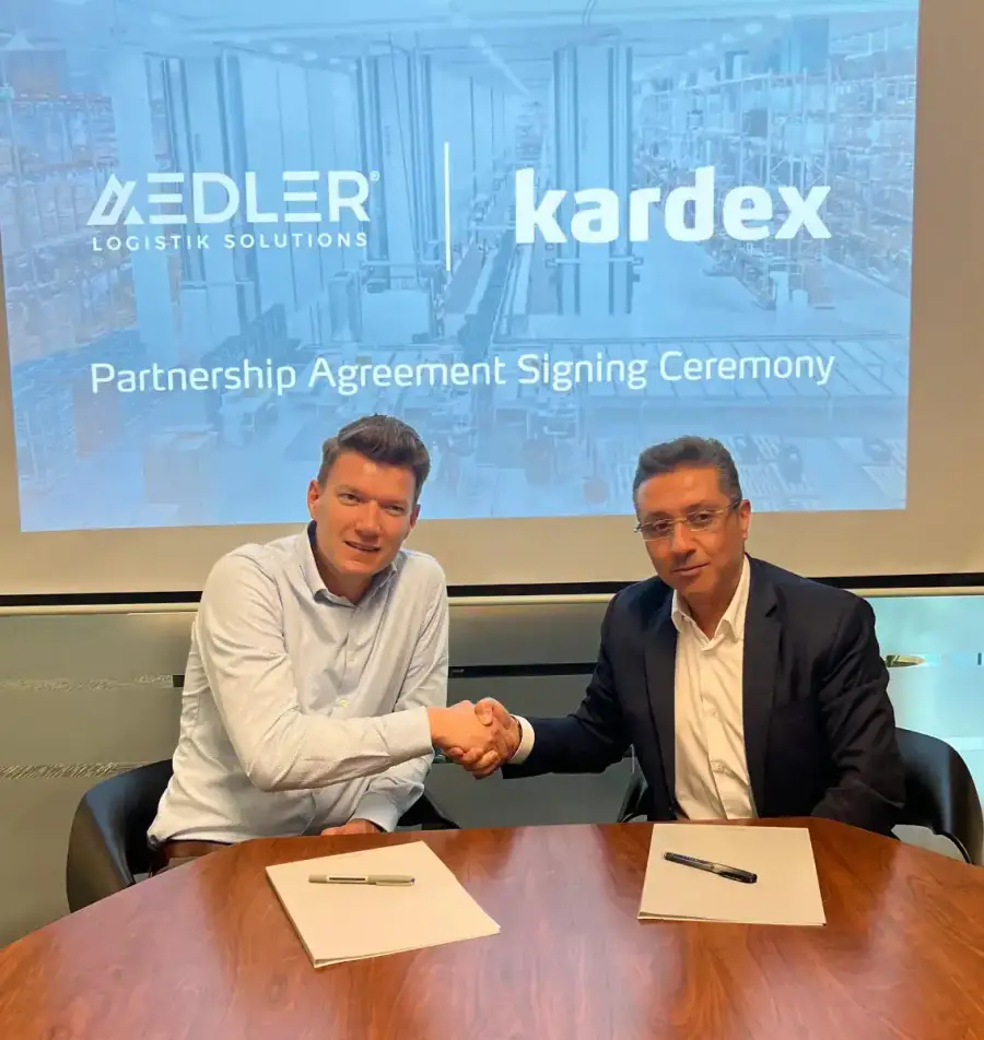 AEDLER and Kardex representatives shaking hands at a signing table under the partnership ceremony screen