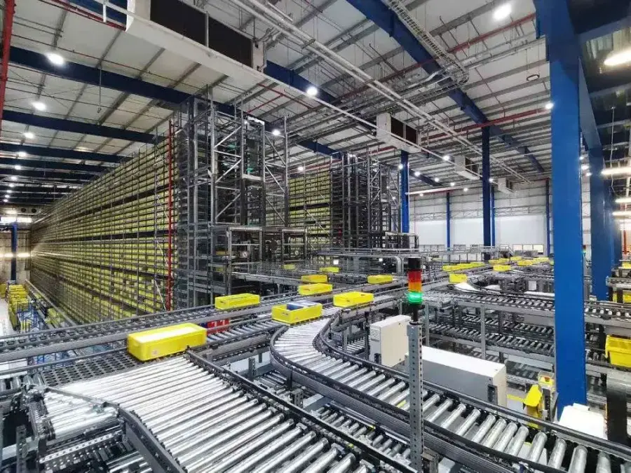 Conveyors carrying yellow totes beside tall shuttle storage racks in the Al Dawaa automated pharmaceutical warehouse, Riyadh