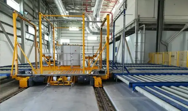 Yellow rail-guided transfer vehicle with roller deck next to blue ULD conveyors at Salalah International Cargo Terminal, Oman