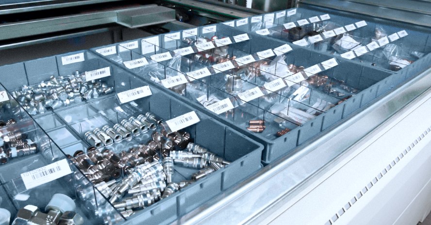 Vertical lift module tray with barcode-labelled bins holding small metal fittings and connectors